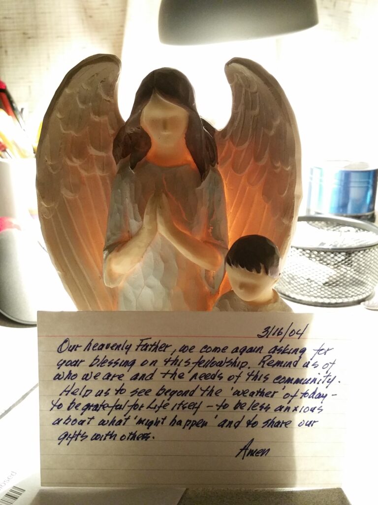 index card prayer propped up against a statue of an angel and child praying